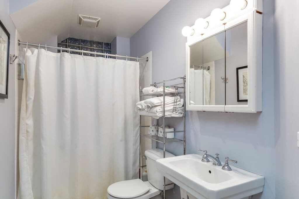A bathroom with a shower curtain, a toilet, a sink with a mirror, and a towel rack with folded towels.