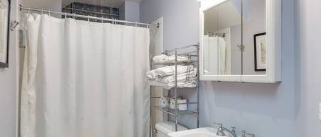 Un baño con cortina de ducha, inodoro, lavabo con espejo y toallero con toallas dobladas.