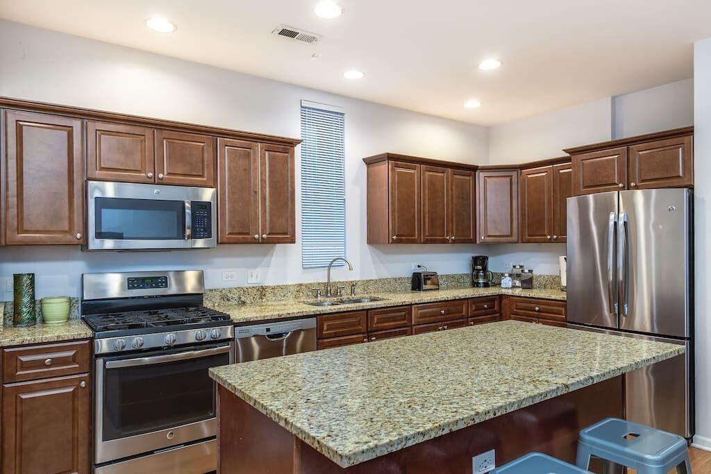 Una cocina moderna con encimeras de granito, electrodomésticos de acero inoxidable y armarios de madera.