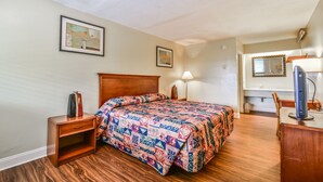 A bedroom with a wooden bed, a nightstand, a desk, a lamp, and a mirror. - Economy Hotel Atlanta   (Atlanta)