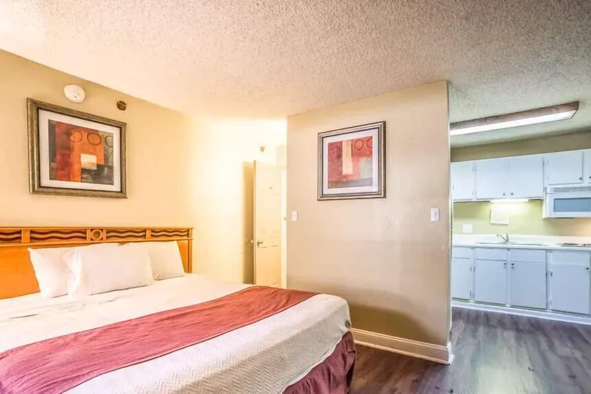 A hotel room with a bed, a kitchenette, and two framed pictures on the wall.