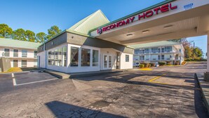 Un hotel con una marquesina de gasolinera, estacionamiento y un edificio de varios pisos y balcones.
