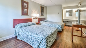 Habitación de hotel con dos camas, cabecero de madera, mesitas de noche con lámparas, un espejo y un escritorio de madera.