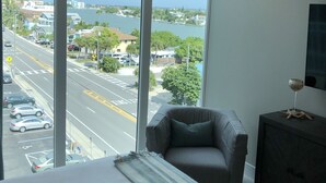Quarto de hotel com uma grande janela que oferece vista para uma rua movimentada e um corpo de água.