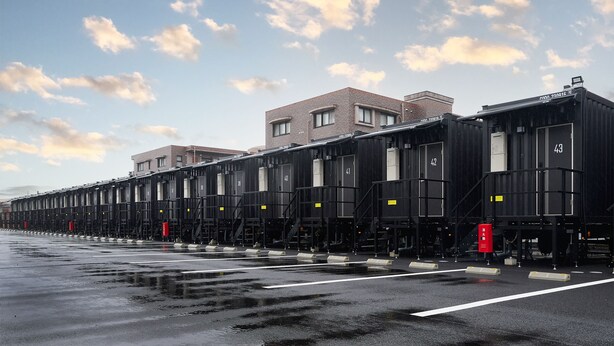 A row of industrial-style buildings with numbered sections, a wet ground, and a partly cloudy sky. - HOTEL R9 The Yard Matsusaka (Matsusaka)
