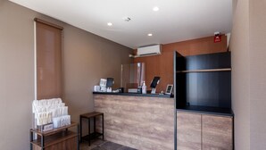 A reception area with a wooden counter, a small seating area, and a trash bin. - HOTEL R9 The Yard Matsusaka (Matsusaka)