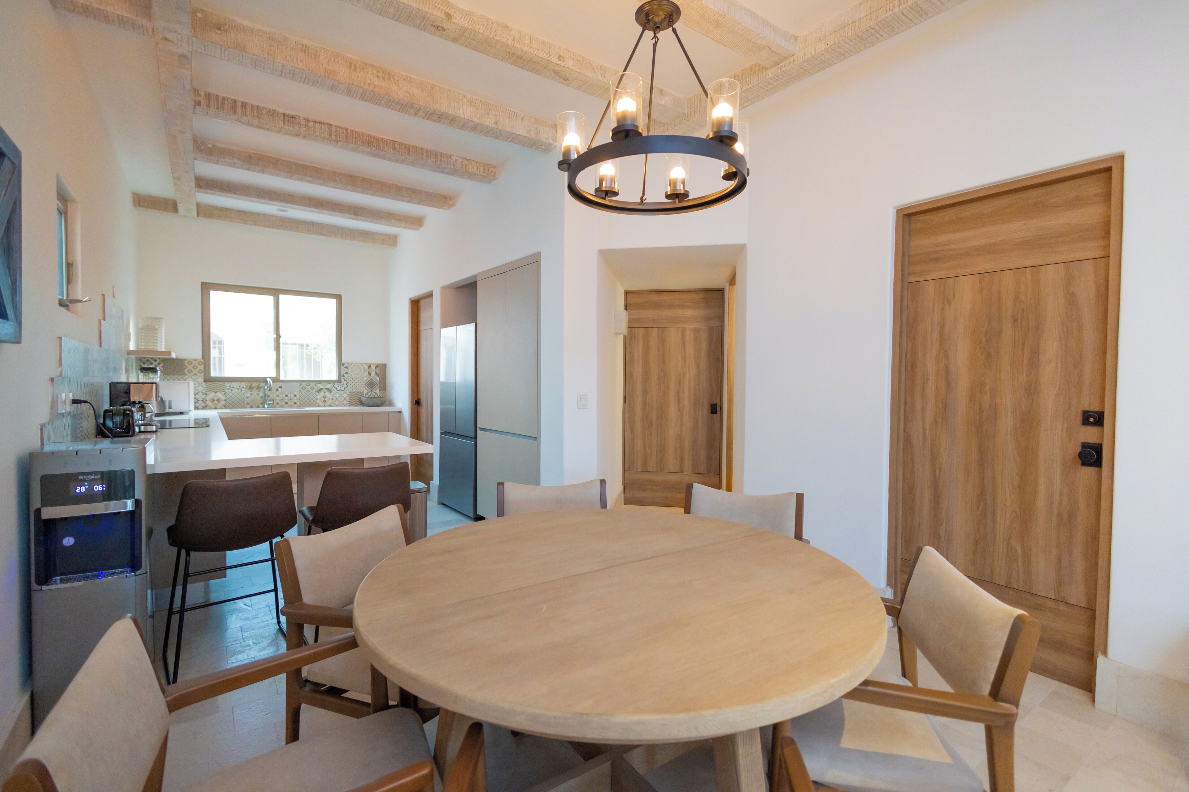 Uma cozinha moderna com uma ilha central, uma área de jantar com mesa e cadeiras redondas, e uma porta de madeira.