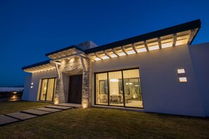 Ein modernes Haus mit Steineingang, großen Glasfenstern und einer gut beleuchteten Außenfassade im Dämmerlicht.