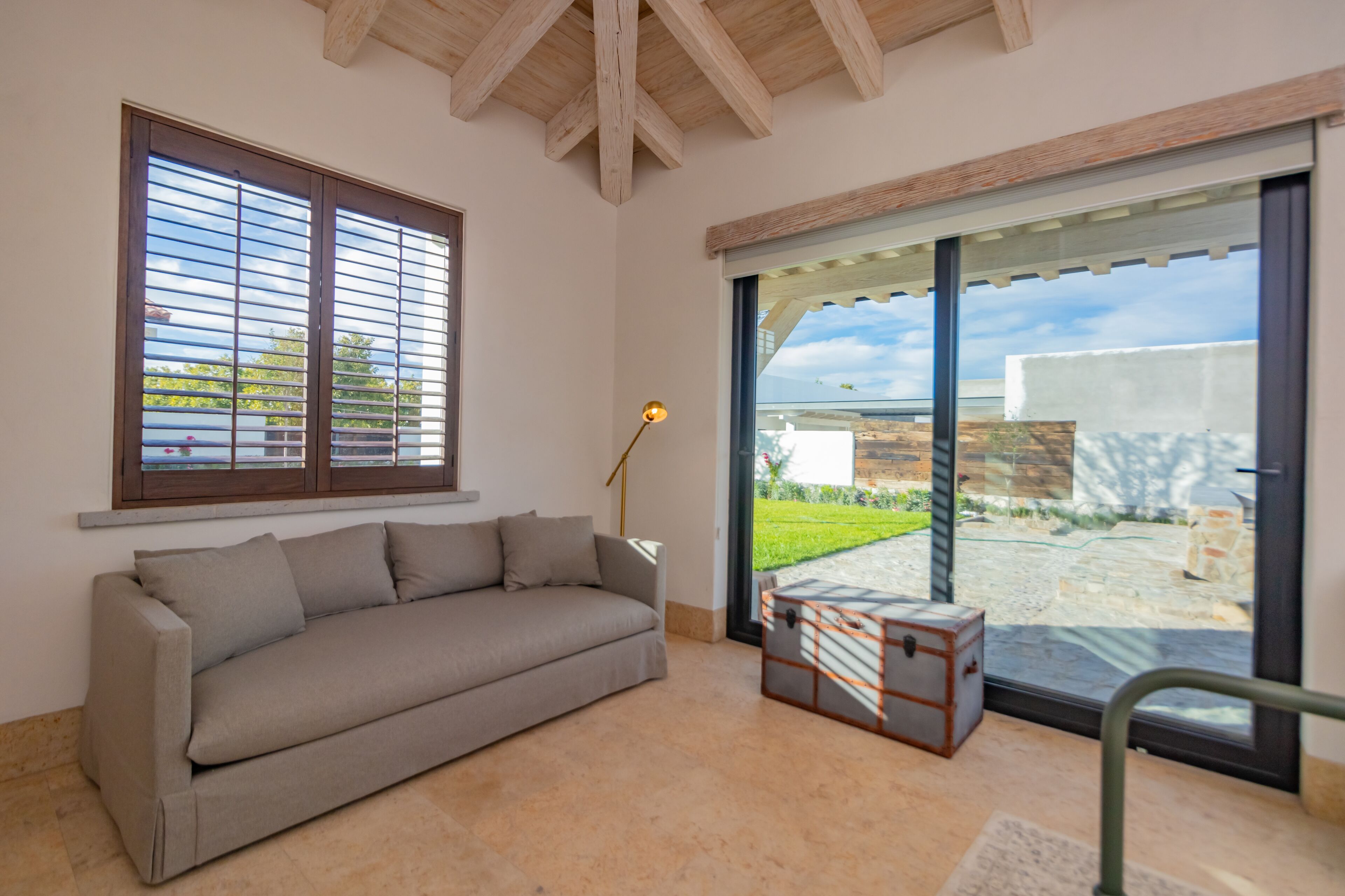 A modern living room with a beige sofa, a vintage suitcase, and a large sliding glass door leading to an outdoor area.