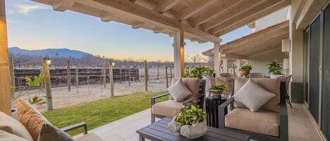 A covered patio area with outdoor furniture, a view of a fenced yard, and a mountain in the background.