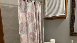 A bathroom with a shower curtain, toilet, sink, and a window with blinds.