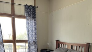 A bedroom with a wooden bed, a nightstand, a window with curtains, and a view of the outdoors.