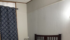 A bedroom with a wooden bed, a chair, a nightstand, and a patterned curtain.