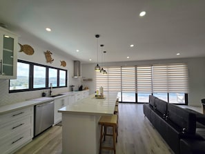 A modern kitchen with a large island, white cabinetry, and a view of the ocean.