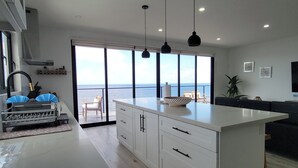 Et moderne køkken med en stor ø, et spiseområde med havudsigt, og en opholdsstue med sofa og TV.