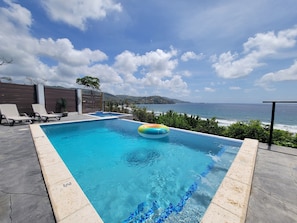 Ein rechteckiger Pool mit klarem, blauem Wasser, einem schwimmenden Ring und Blick auf den Ozean.