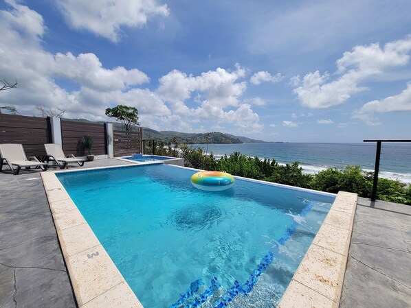 A rectangular swimming pool with clear blue water, a floating ring, and a view of the ocean.