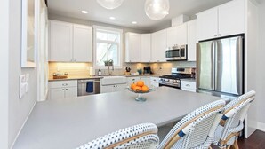 A modern kitchen with white cabinets, stainless steel appliances, and a central island with a fruit bowl. - Modern Cottage "M" Luxury home w/hot tub, community pool-walk to town & beach (New Buffalo)