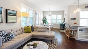 A modern living room with a sectional sofa, a coffee table, and a dining area with chairs. - Modern Cottage "M" Luxury home w/hot tub, community pool-walk to town & beach (New Buffalo)