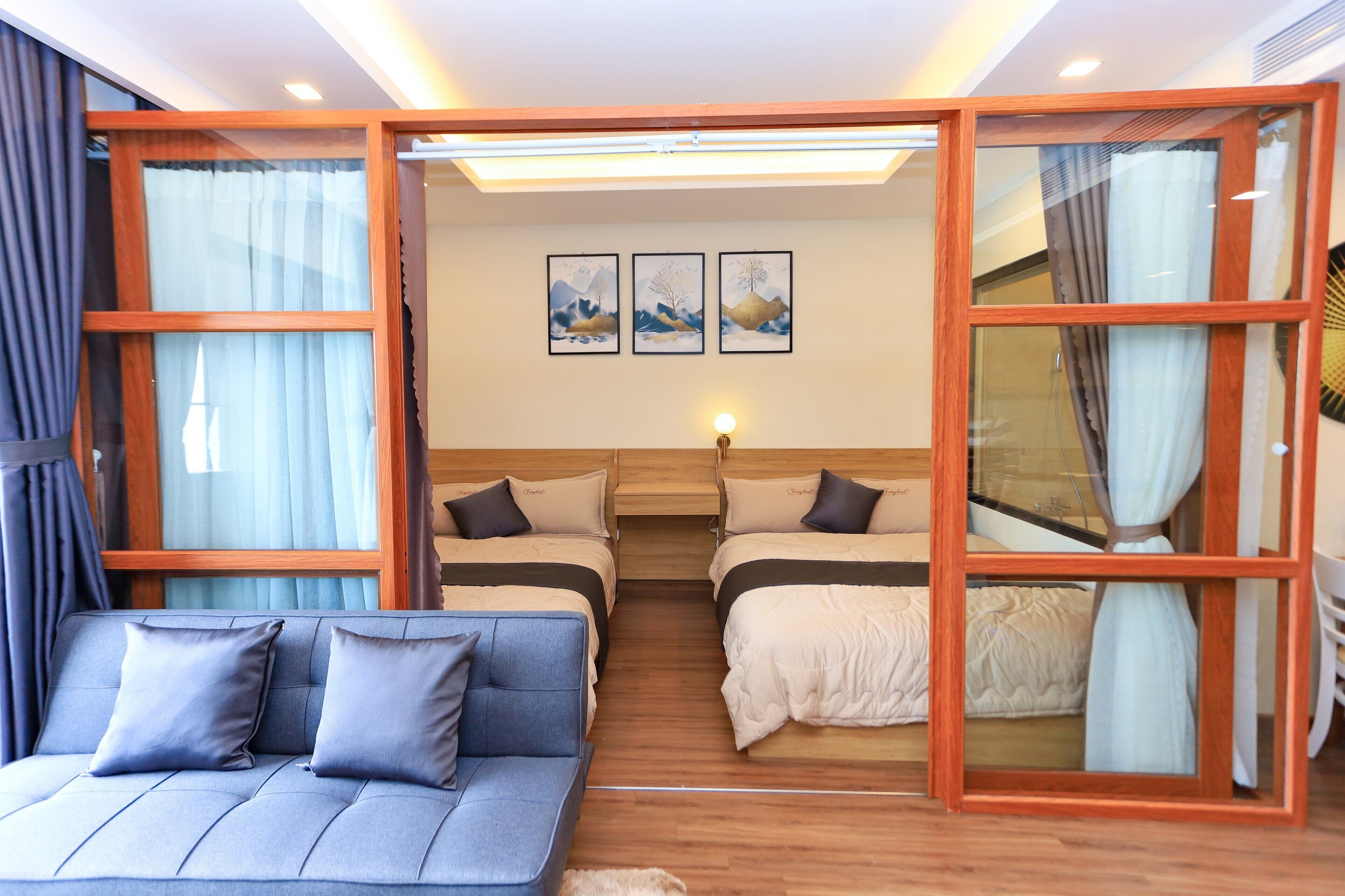 A room with a sofa, two beds, and a wall with three framed pictures.
