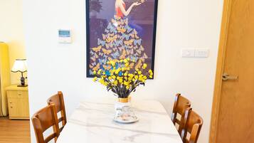 Ein Essbereich mit einem weißen Tisch, zwei Holzstühlen, einer Vase mit gelben Blumen, einer Uhr und einem gerahmten Kunstwerk an der Wand.