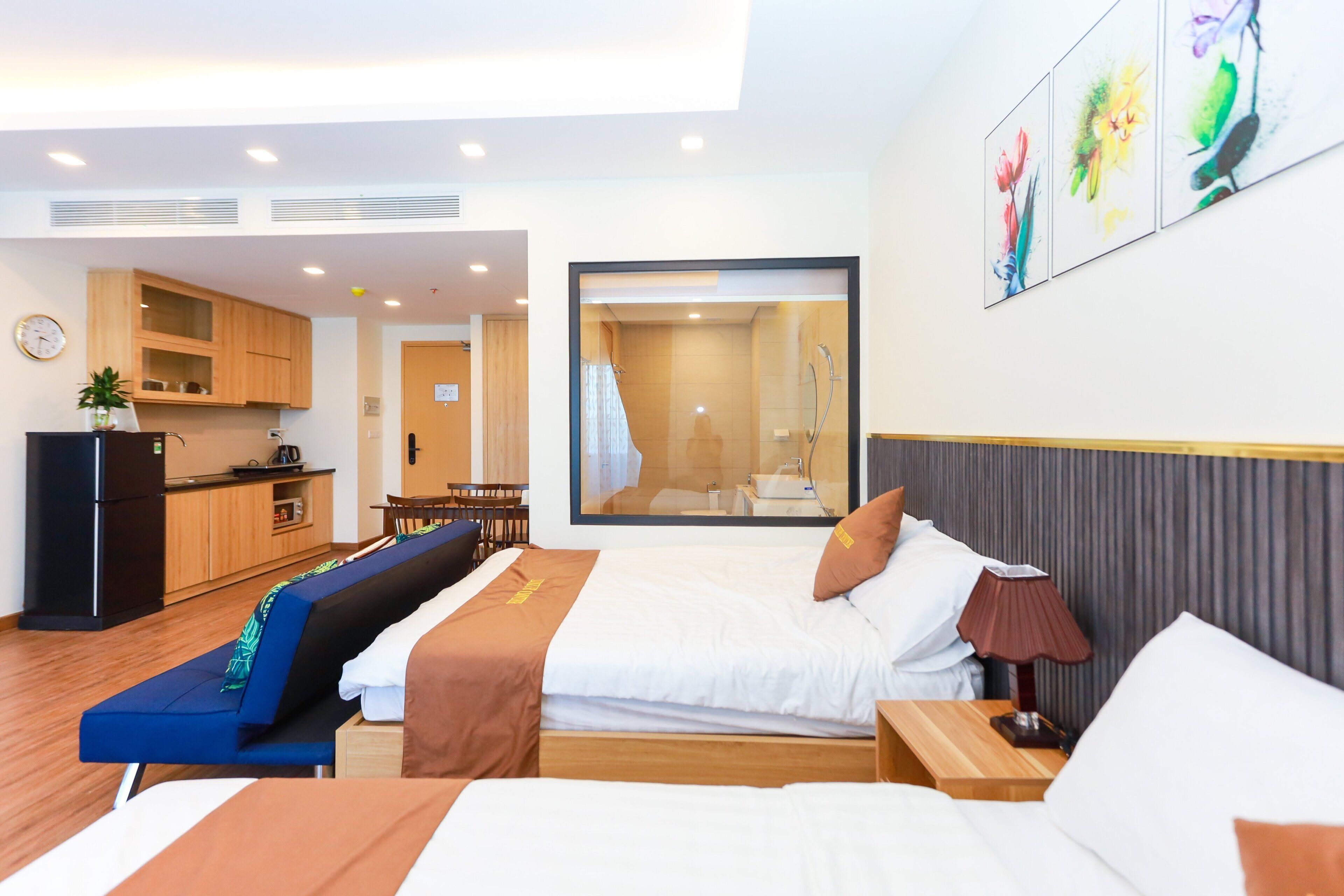 Ein Hotelzimmer mit Bett, Nachttischen, Schreibtisch, Sessel, einer Couch, einer Küchenzeile und einem Badezimmer mit Dusche.