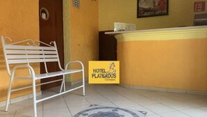 A hotel reception area with a bench, a reception desk, and a sign for 'Hotel Plateados'.