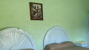 A room with two beds with white headboards, green walls, and a framed picture on the wall.