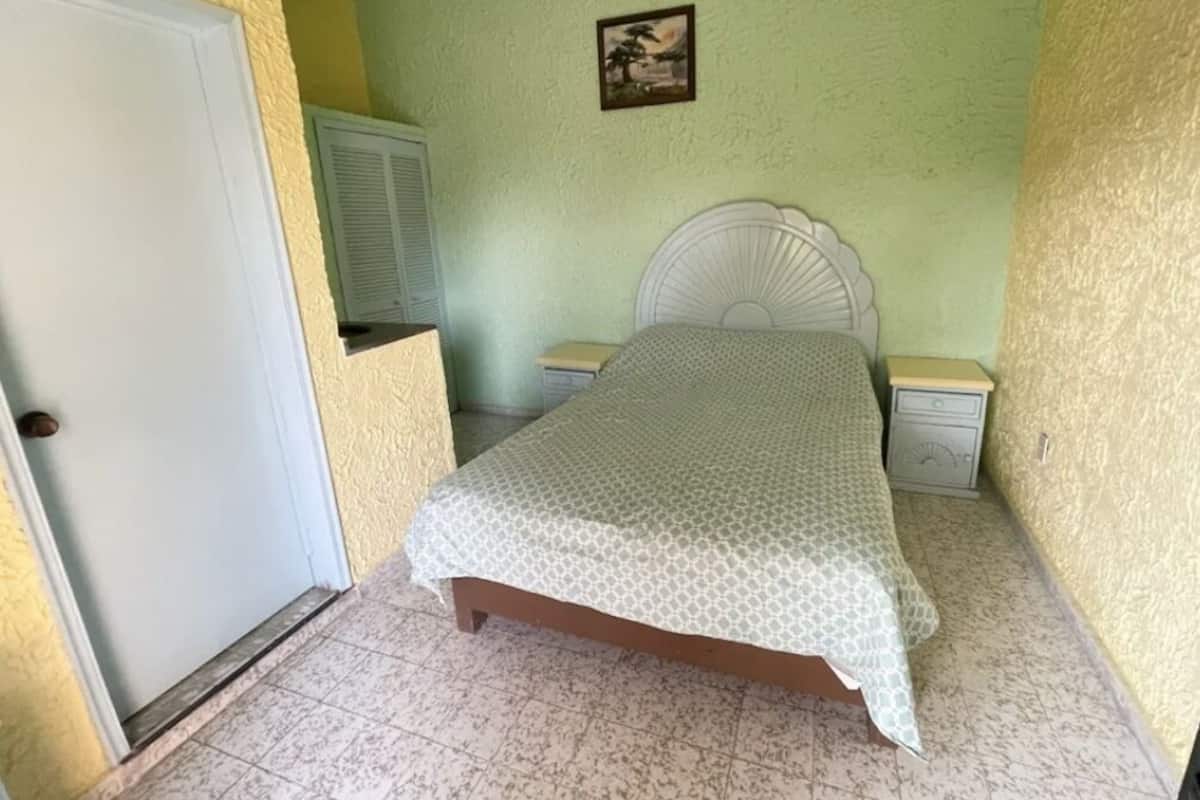Un dormitorio con cama, mesitas de noche, una puerta y un cuadro colgado en la pared.