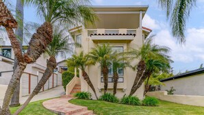 Una casa de dos pisos con un camino de entrada curvo, palmeras y una pequeña escalera que conduce a la entrada.