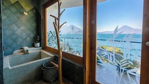 Un baño con bañera, ventana con vista a un paisaje costero y una planta decorativa.