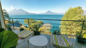 Un balcón con dos sillas y una mesa pequeña, con vista a un cuerpo de agua y montañas.