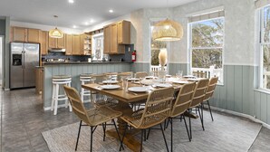 Une cuisine moderne avec des meubles en bois, un réfrigérateur en acier inoxydable et un coin repas comprenant des chaises en osier et une table en bois.