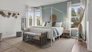 Une chambre à coucher avec un lit à baldaquin, un berceau, une table de chevet, une fenêtre avec des rideaux et une vue sur l’extérieur.