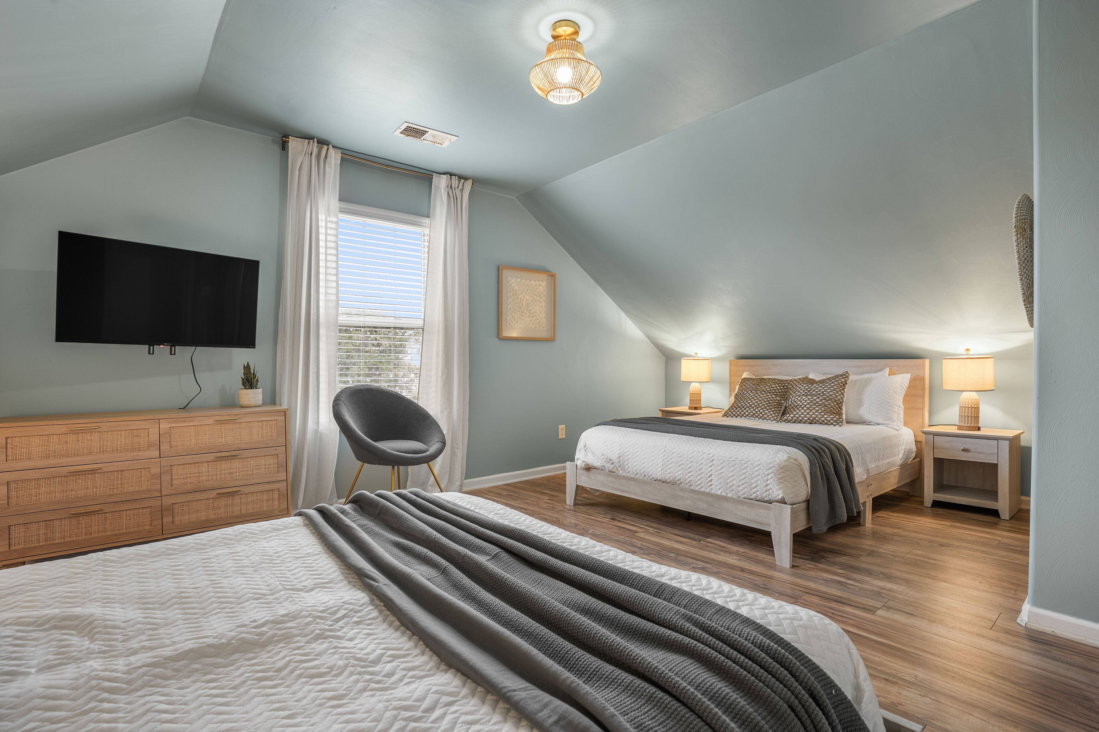 A bedroom with a bed, bedside tables, a TV, a chair, and a window with curtains.