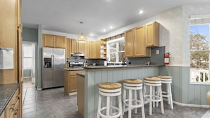 Une cuisine moderne avec des meubles en bois, un réfrigérateur en acier inoxydable, une cuisinière à gaz et un coin bar avec des tabourets.