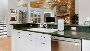 A modern kitchen with a stone accent wall, a built-in dishwasher, and a large window offering a view of the outdoors. - Amazing Views / Hot Tub / 15 mins to Wineries / 3200 sq ft (Wintergreen Resort)