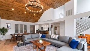A spacious living room with a wooden ceiling, a large gray sofa, a wooden coffee table, and a chandelier. - Amazing Views / Hot Tub / 15 mins to Wineries / 3200 sq ft (Wintergreen Resort)