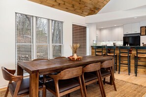 A modern kitchen with white cabinets, a dark countertop, and a large TV.