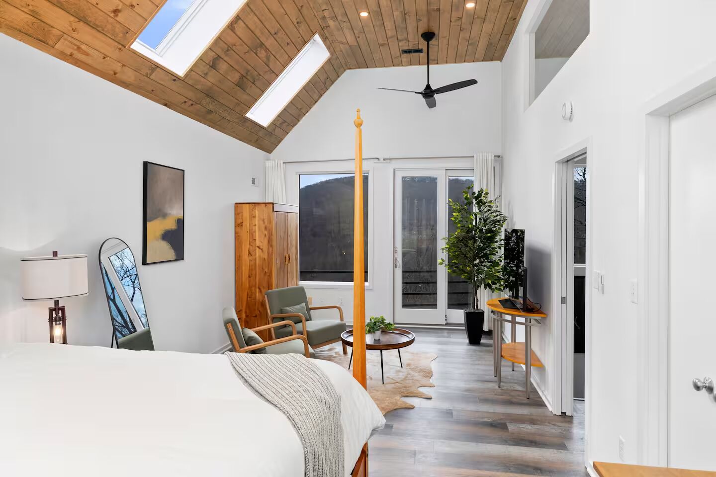 A modern bedroom with a large bed, a wooden wardrobe, a ceiling fan, and a view of the outdoors through a sliding glass door.