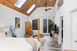 Une chambre moderne avec un grand lit, une armoire en bois, un ventilateur de plafond et une vue sur l’extérieur grâce à une porte-fenêtre coulissante.