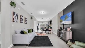A modern living room with a grey sofa, a round coffee table, and a TV mounted on the wall. - Uniquely Chic home near Disney! (Kissimmee)