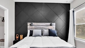 A modern bedroom with a dark headboard, a wooden accent panel, and a neatly made bed with pillows. - Uniquely Chic home near Disney! (Kissimmee)