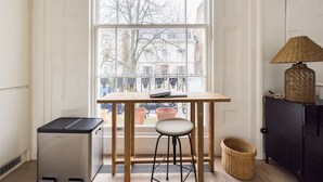 Une cuisine de taille réduite, dotée d’une fenêtre, d’une petite table, d’un tabouret, d’un meuble et d’un réfrigérateur compact.