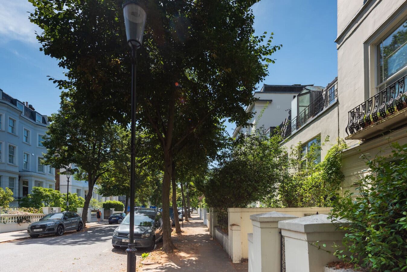 A tree-lined street with parked cars and a building with balconies.