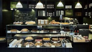 Une vitrine de boulangerie présentant diverses pâtisseries et gâteaux, un menu écrit à la craie et des lampes suspendues.