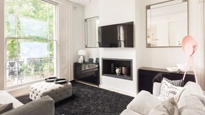 Un salon moderne doté d’une grande fenêtre, d’un téléviseur à écran plat, d’une cheminée et d’un tapis noir.