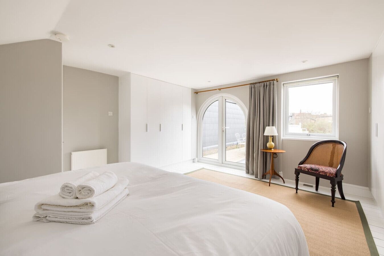 A hotel room with a bed, a chair, a lamp, and a view through a window.