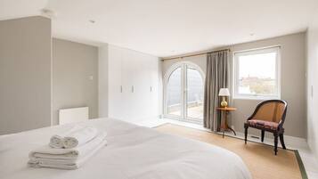 A hotel room with a bed, a chair, a lamp, and a view through a window.