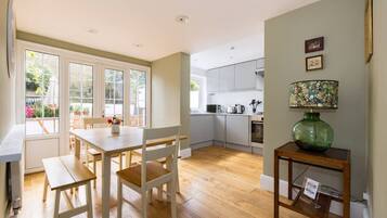 A modern kitchen with white cabinets, a dining area with a wooden table and chairs, and a green vase on a side table.